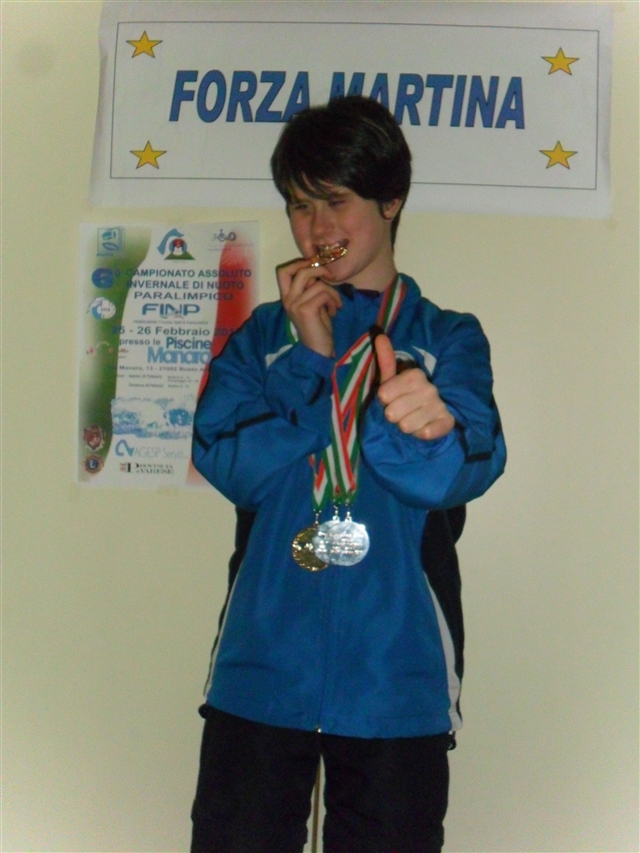 Martina con al collo le medaglie vinte, un cartello con scritto Forza Martina e il manifesto dei 6° CAMPIONATI ASSOLUTI DI NUOTO.